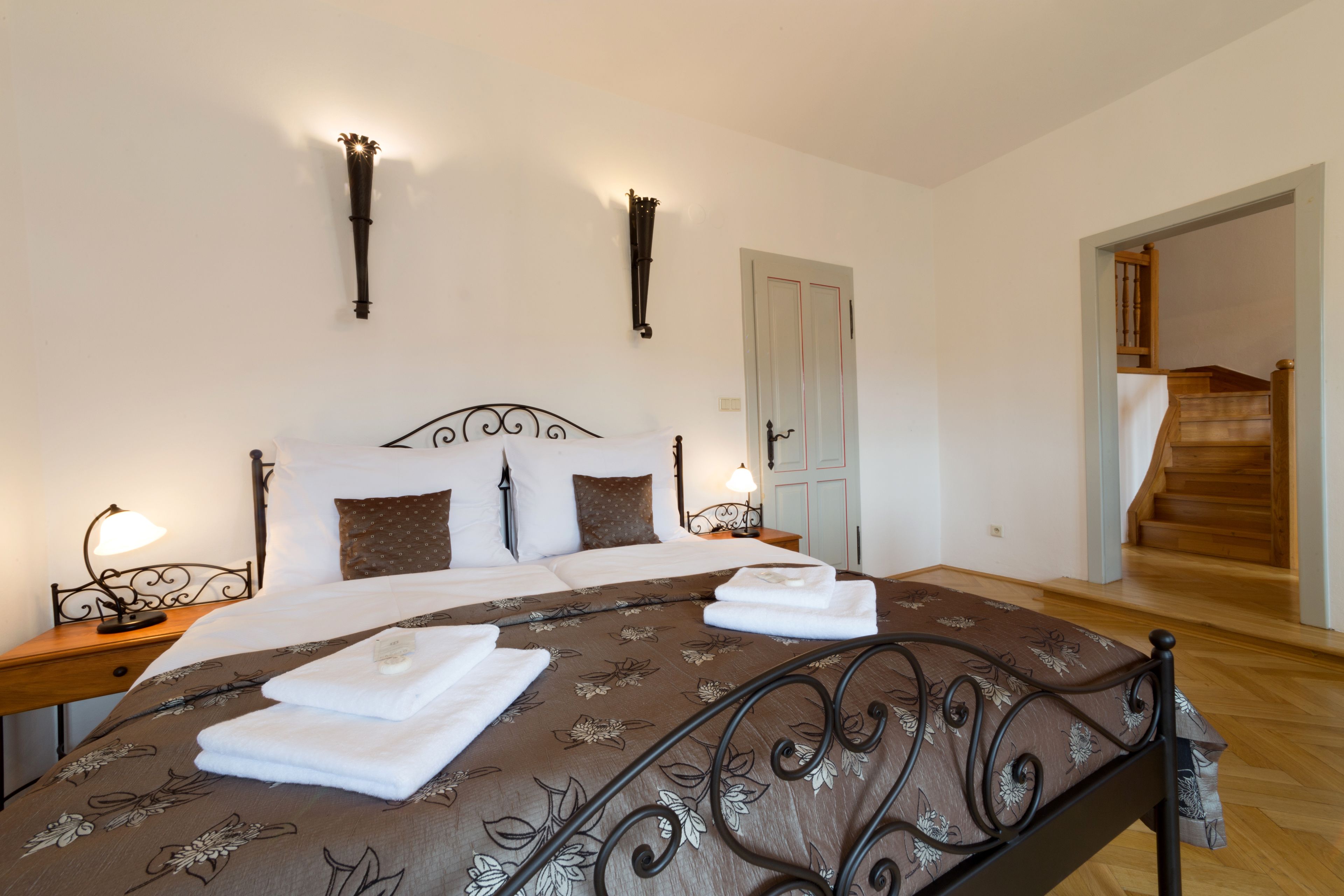 Una cama bien hecha con una colcha floral, dos lámparas de noche y una mesita de noche de madera.
