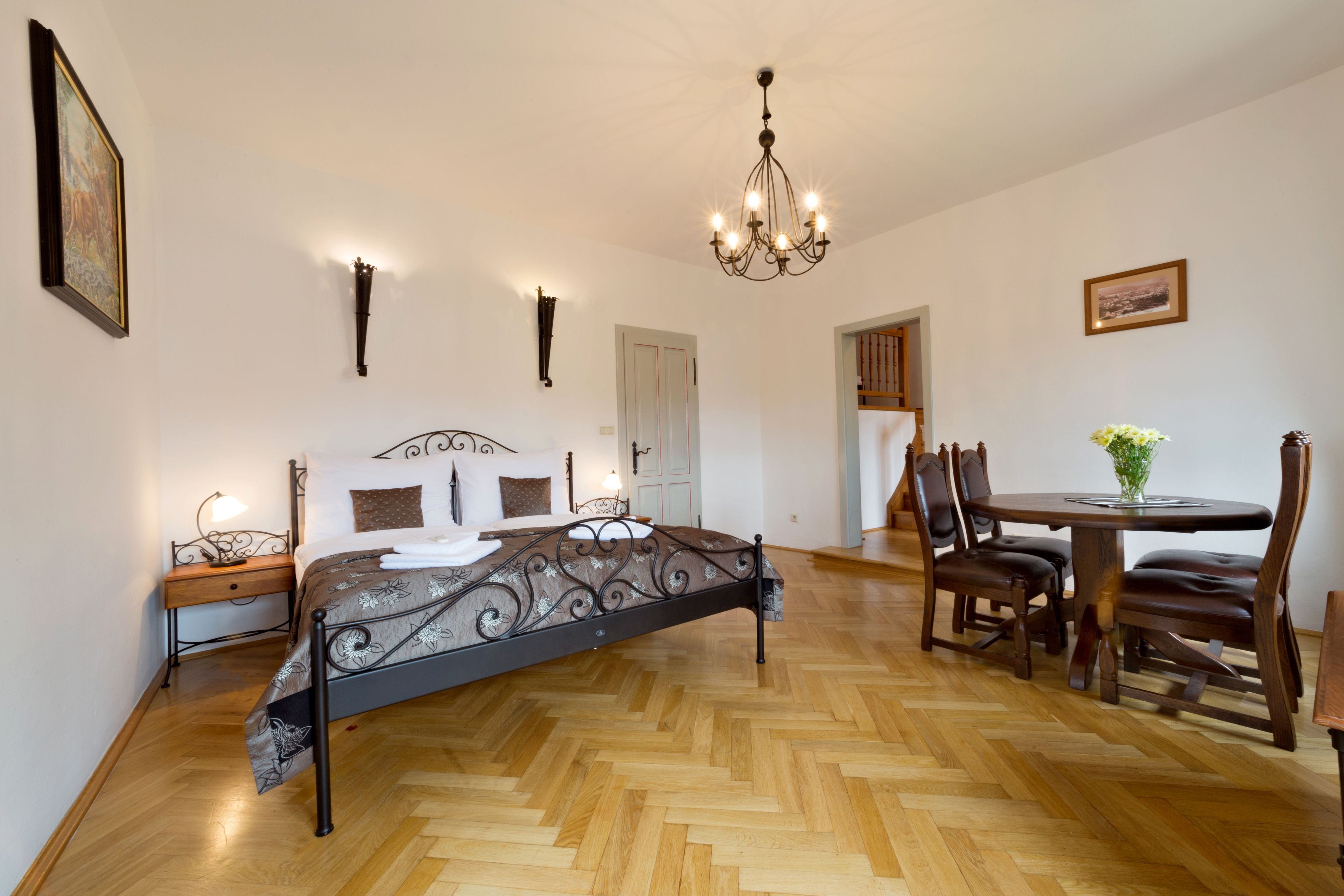 A bedroom with a bed, bedside table, lamp, and a dining area with a table and chairs.