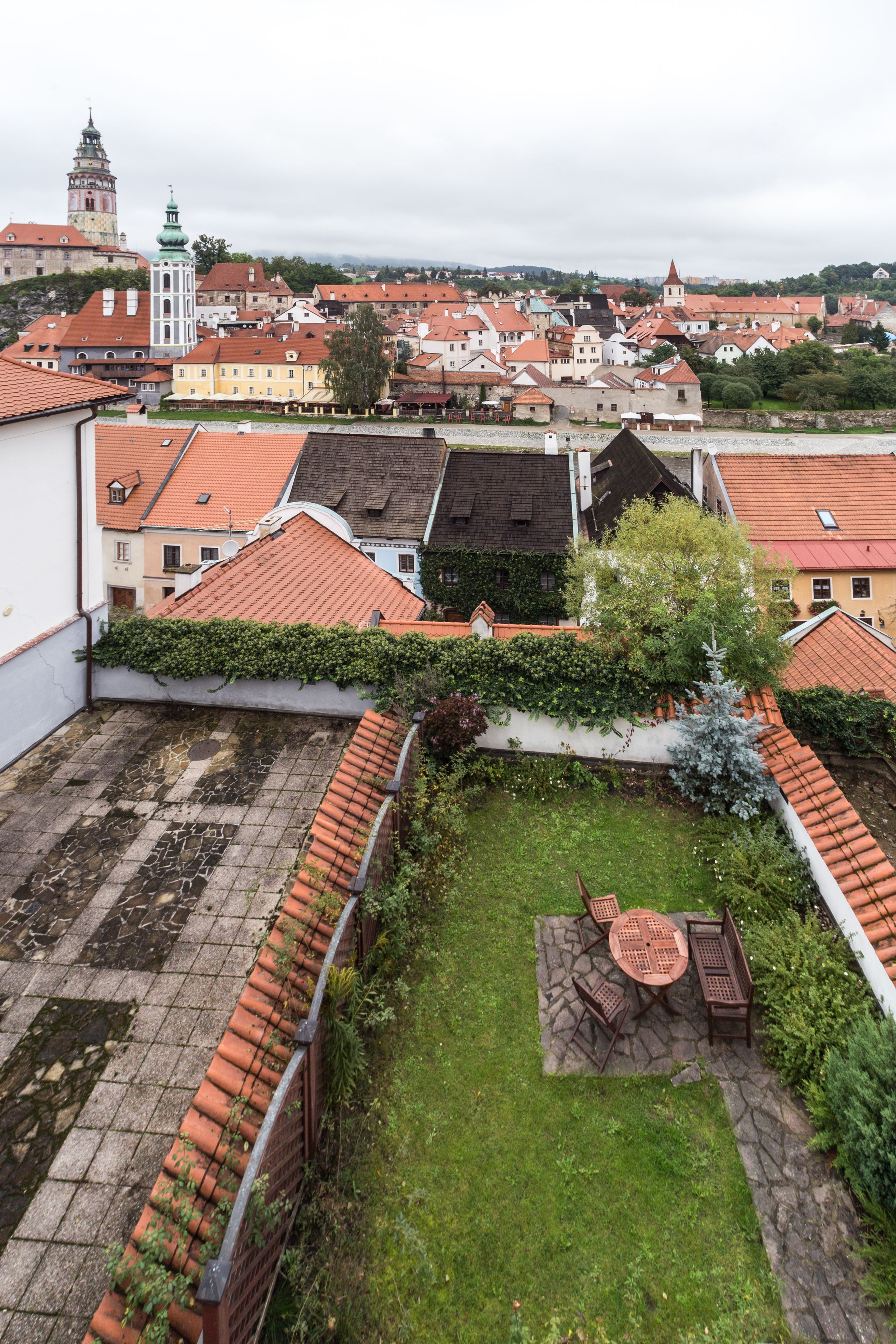 Ein Innenhof mit einem Steintisch und -stühlen, umgeben von einer Backsteinmauer mit Grünpflanzen.