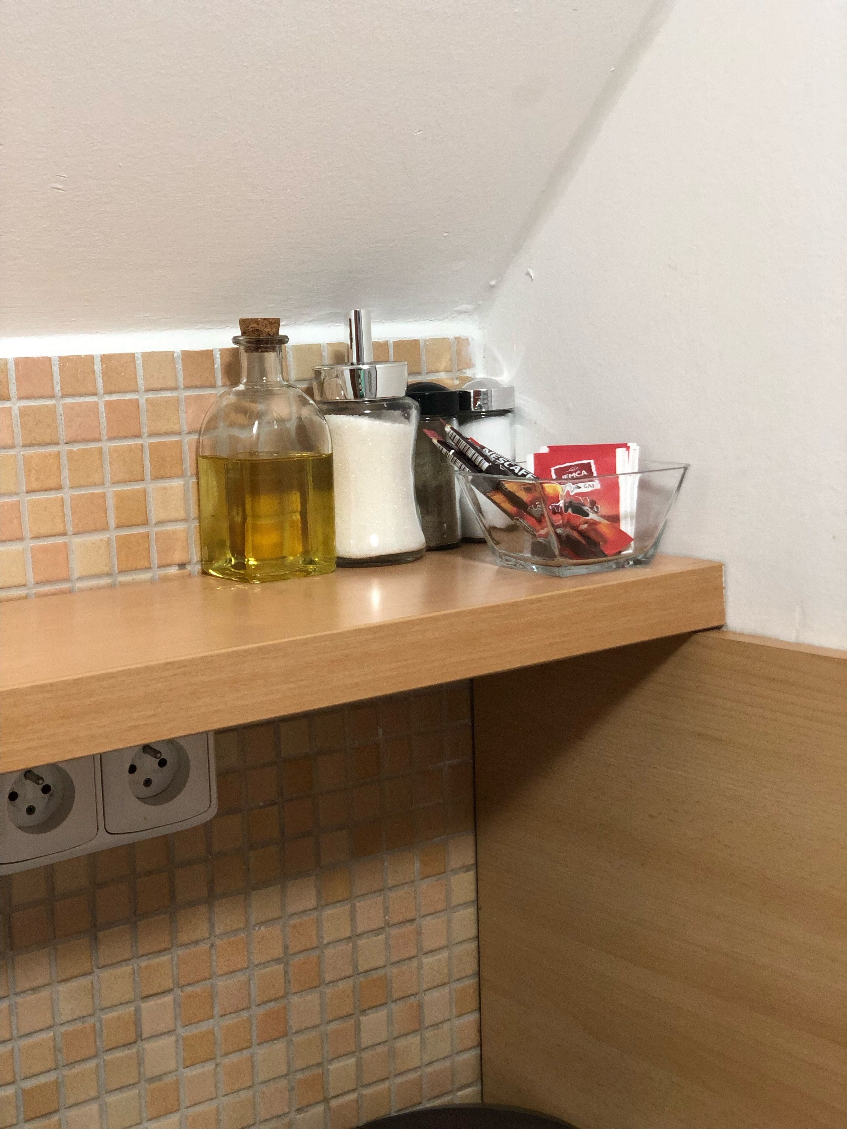 A kitchen counter with a bottle of oil, a salt shaker, a coffee maker, and some coffee pods.
