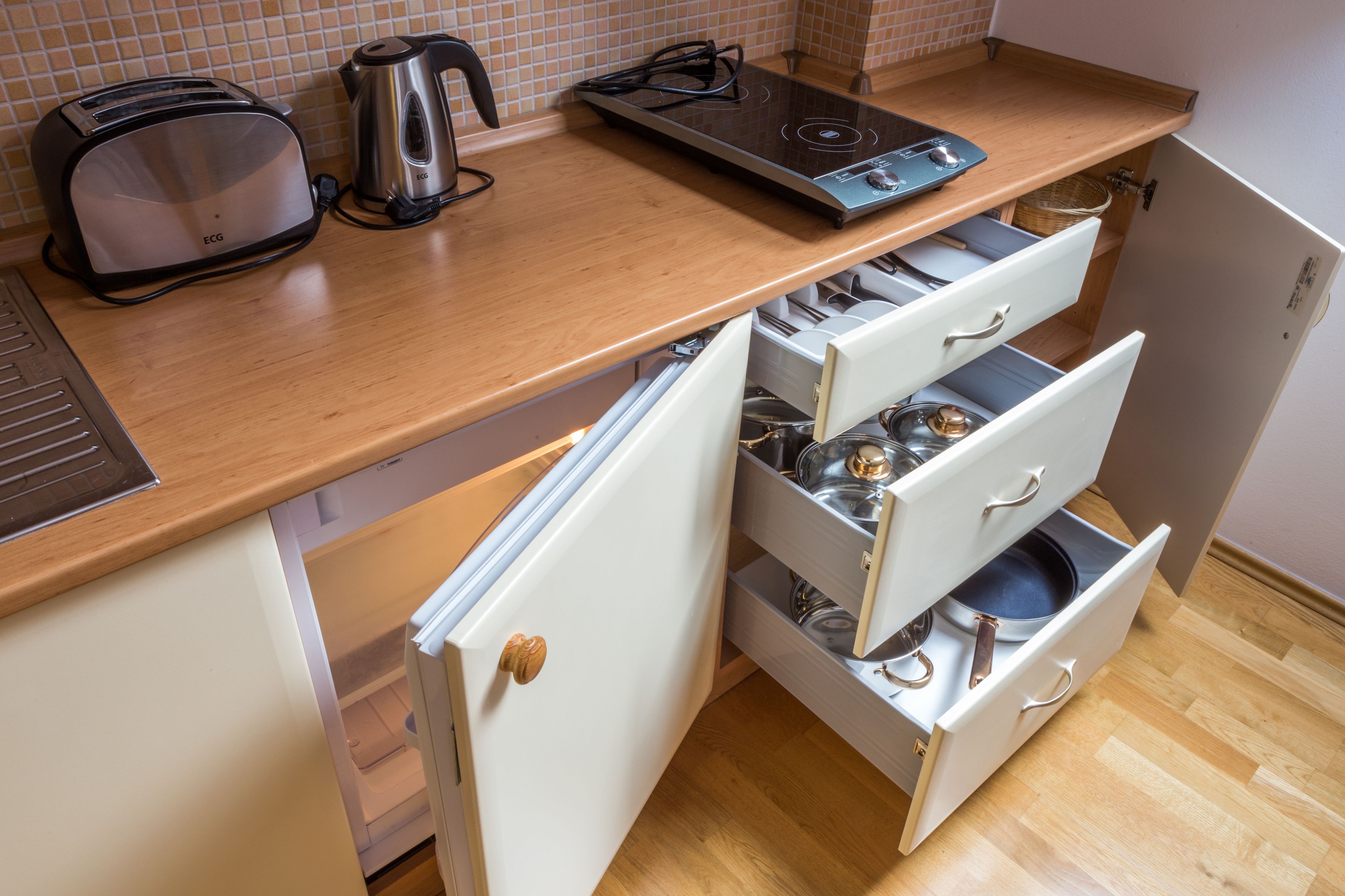 A kitchen with a toaster, kettle, induction cooktop, and a drawer with kitchen utensils.