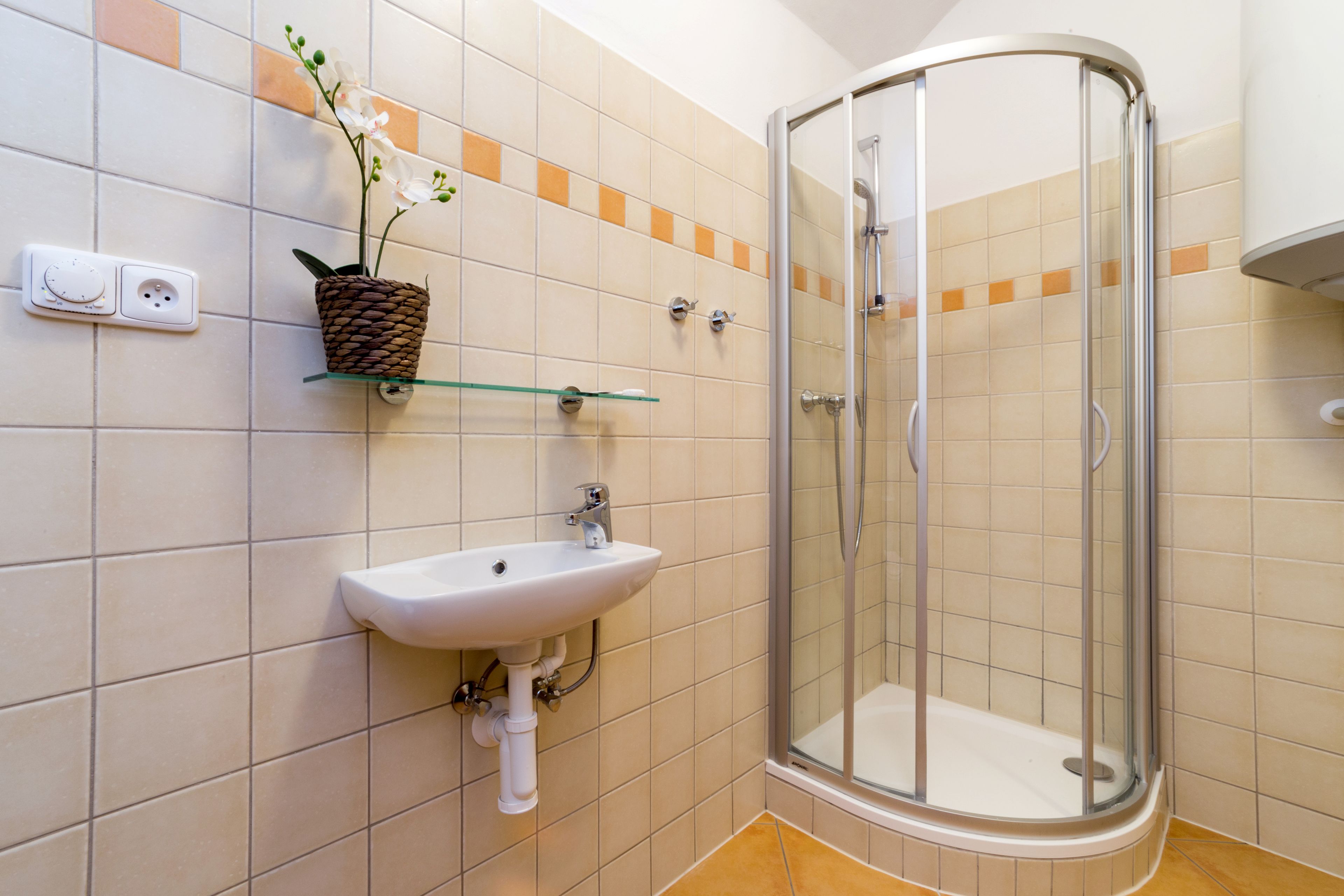 Un baño con cabina de ducha de vidrio, un lavabo con espejo y un enchufe en la pared.