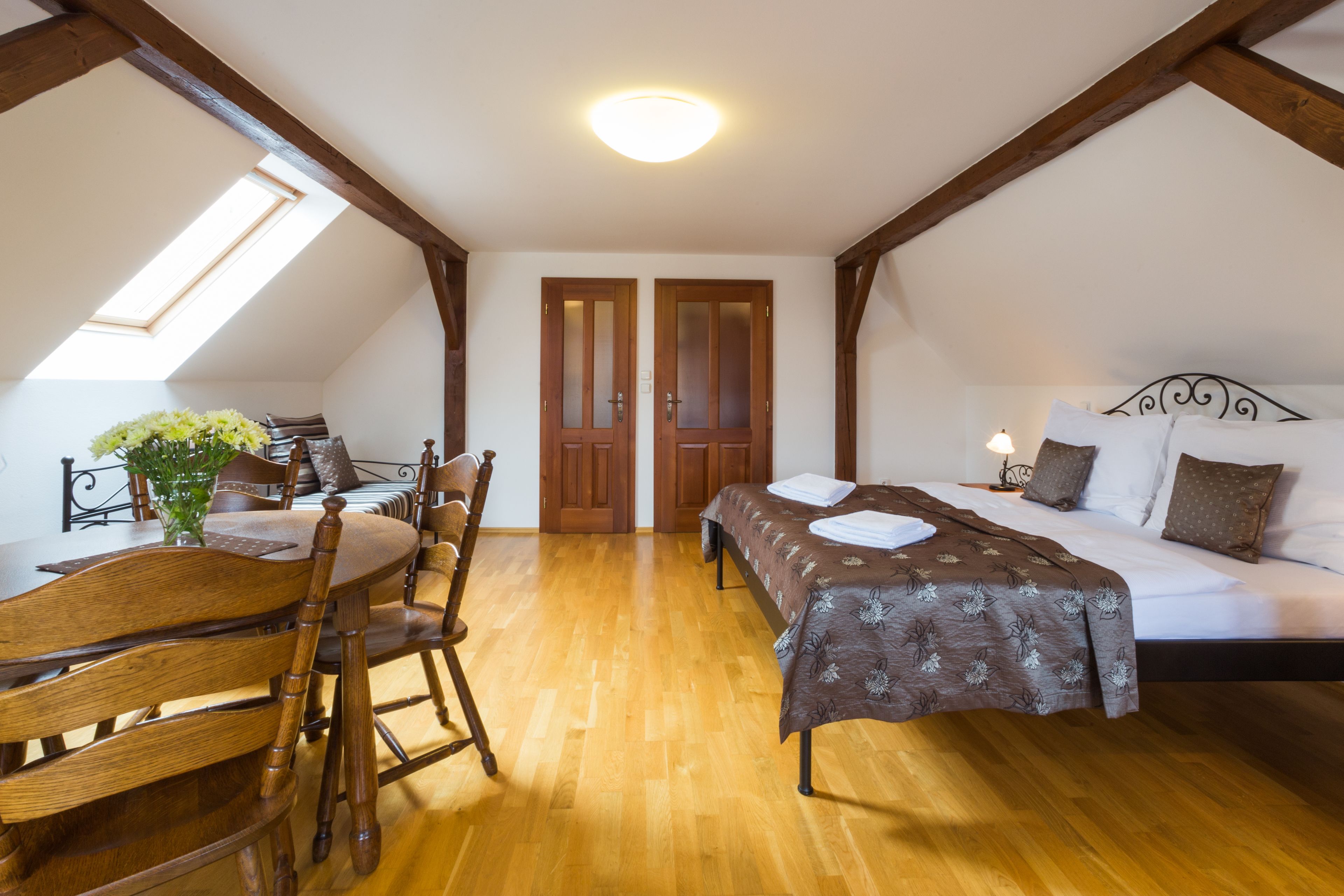 Ein Schlafzimmer mit einem Holzbett, einem Nachttisch, einer Lampe, einem Fenster und einem Essbereich mit Tisch und Stühlen.