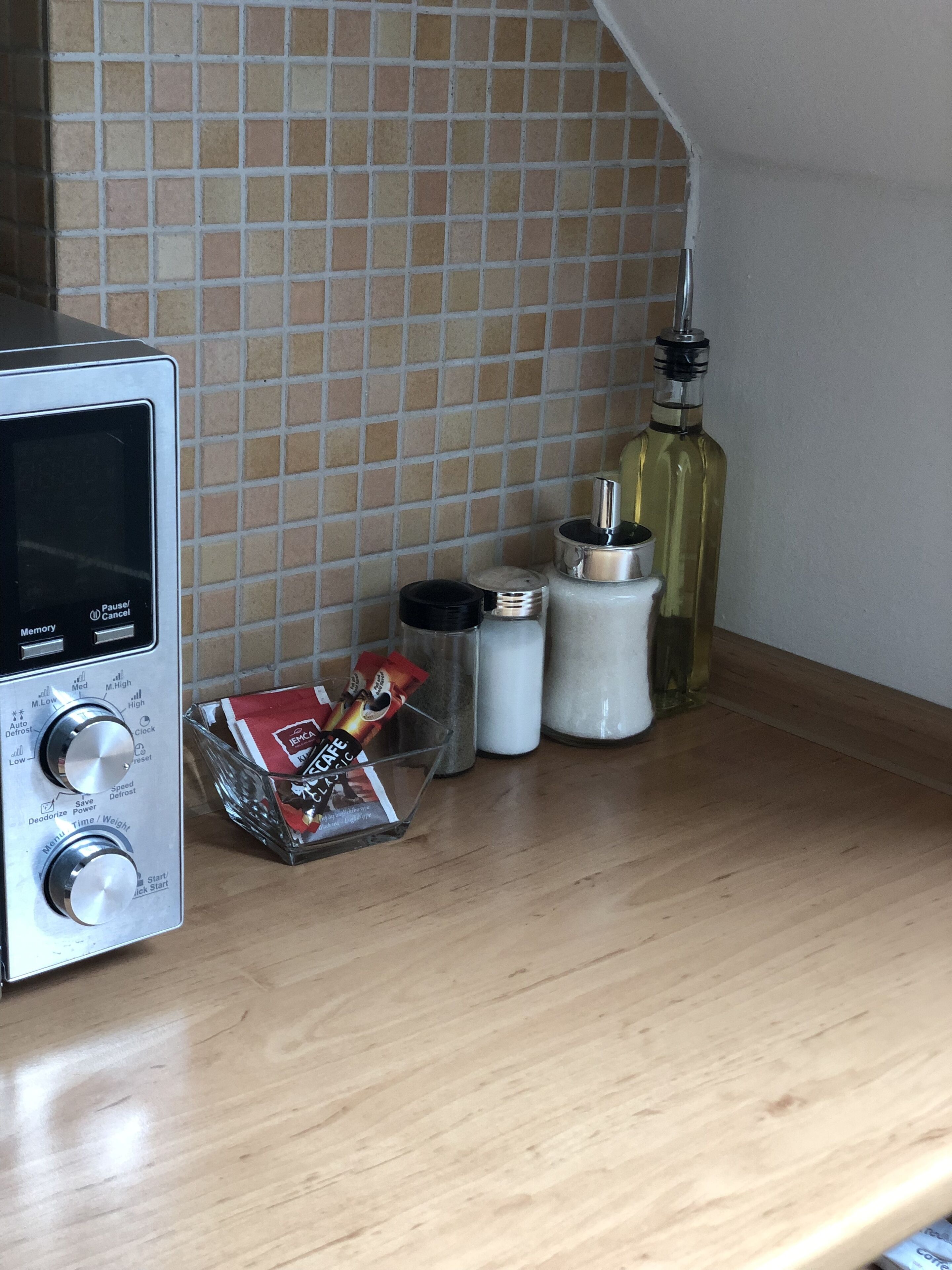 A kitchen counter with a coffee maker, salt and pepper shakers, a bottle of olive oil, and a packet of coffee creamer.