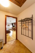 Un pasillo con puerta de madera que da a un comedor, un perchero metálico y suelo de baldosas.