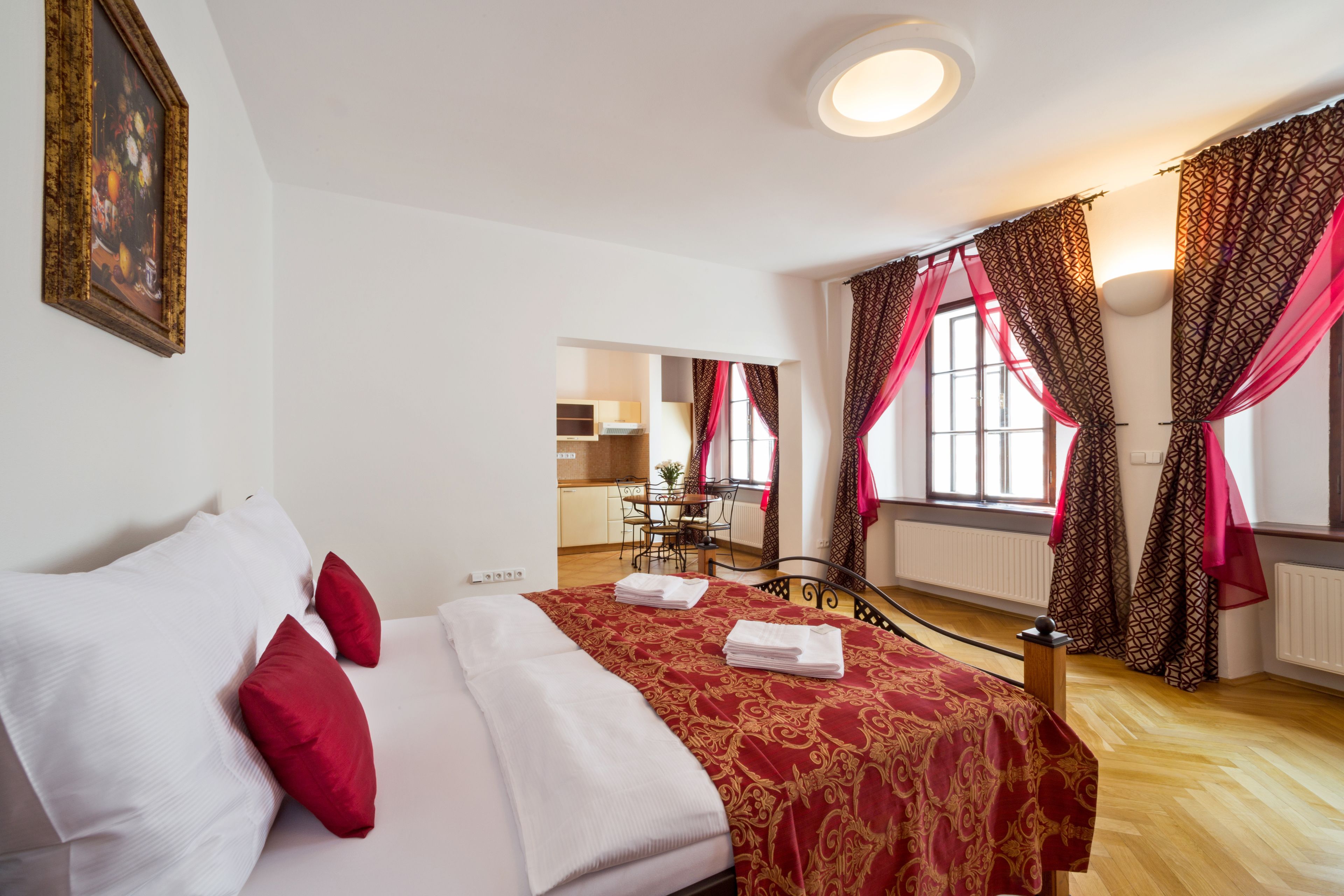 Habitación de hotel con una cama, almohadas rojas y blancas, una colcha de edredón con estampado rojo y dorado, y una ventana con cortinas rojas.