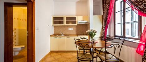 A compact kitchen with a dining area, a window with curtains, and a visible toilet in the adjacent bathroom.