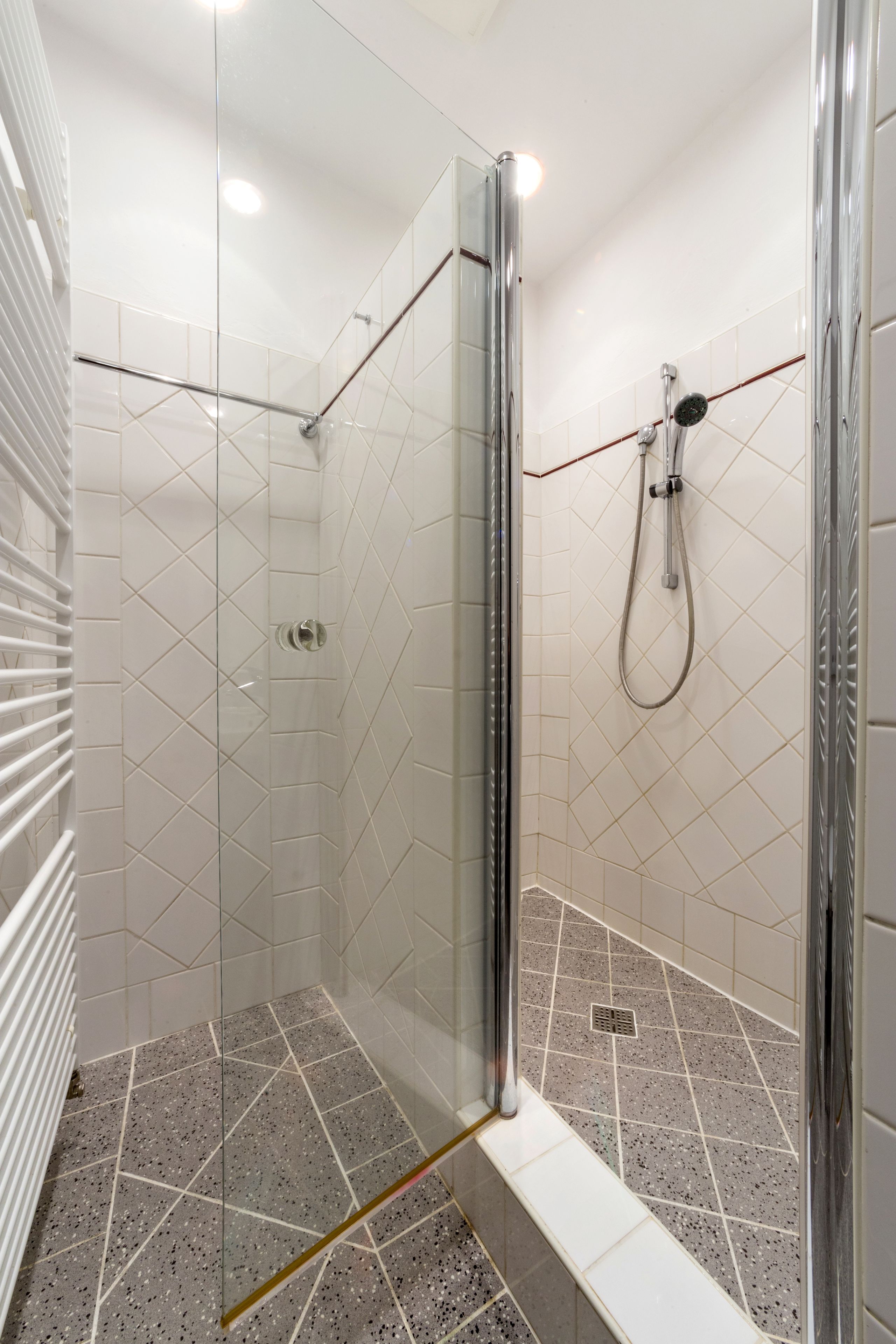 A glass-enclosed shower with a handheld showerhead and a wall-mounted faucet.