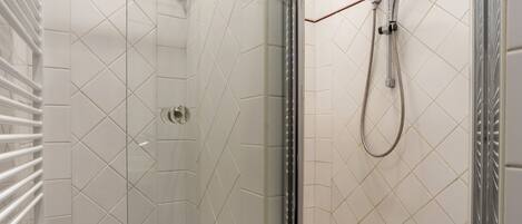 A glass-enclosed shower with a handheld showerhead and a wall-mounted faucet.