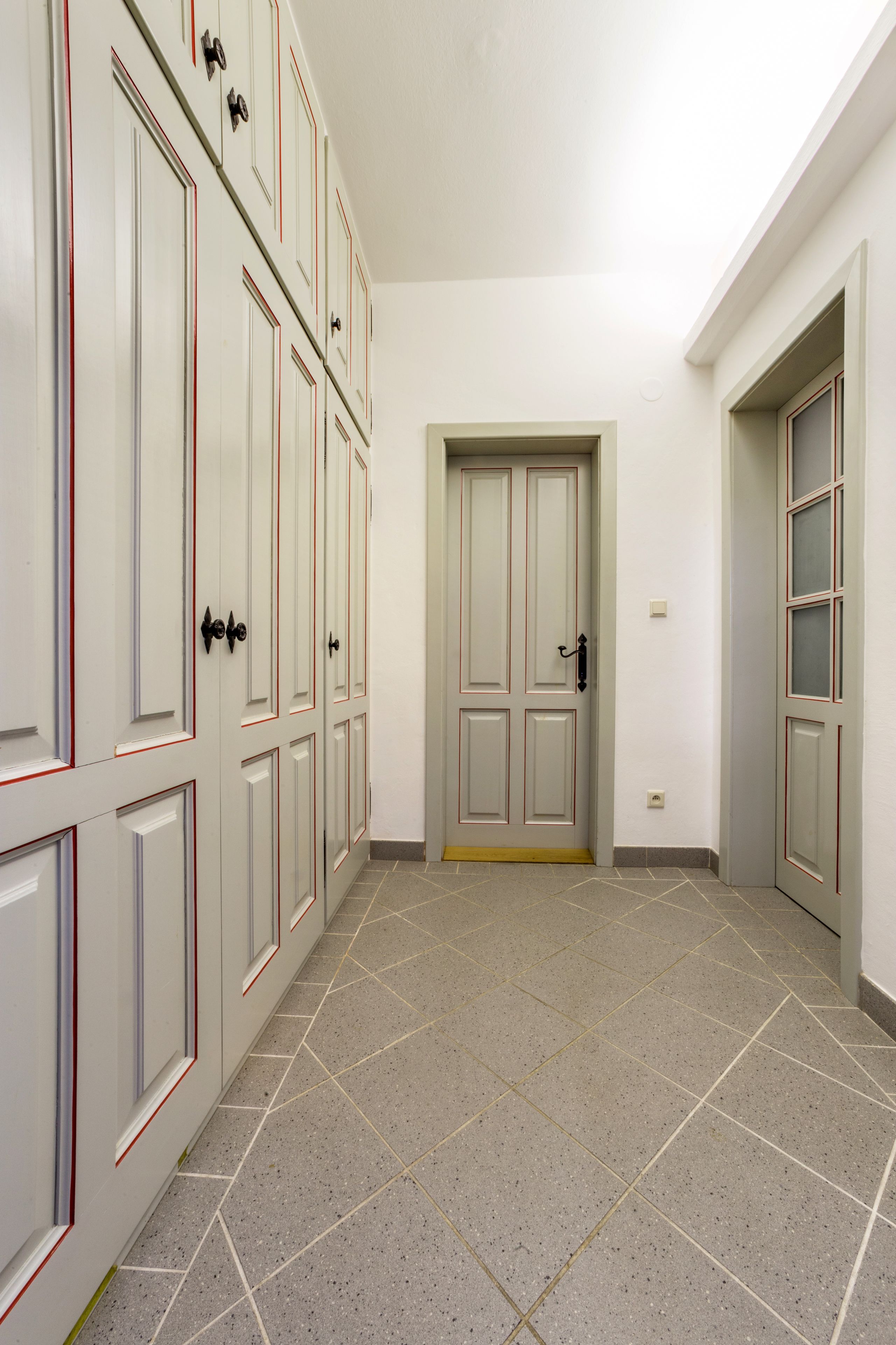 Un pasillo con suelo de baldosas, un juego de puertas dobles y una puerta con panel de vidrio esmerilado.
