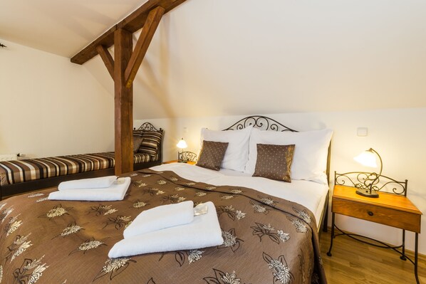 A hotel room with a large bed, a smaller bed, wooden beams, a nightstand with a lamp, and a wall-mounted light. - Vila Krumlov (Cesky Krumlov)