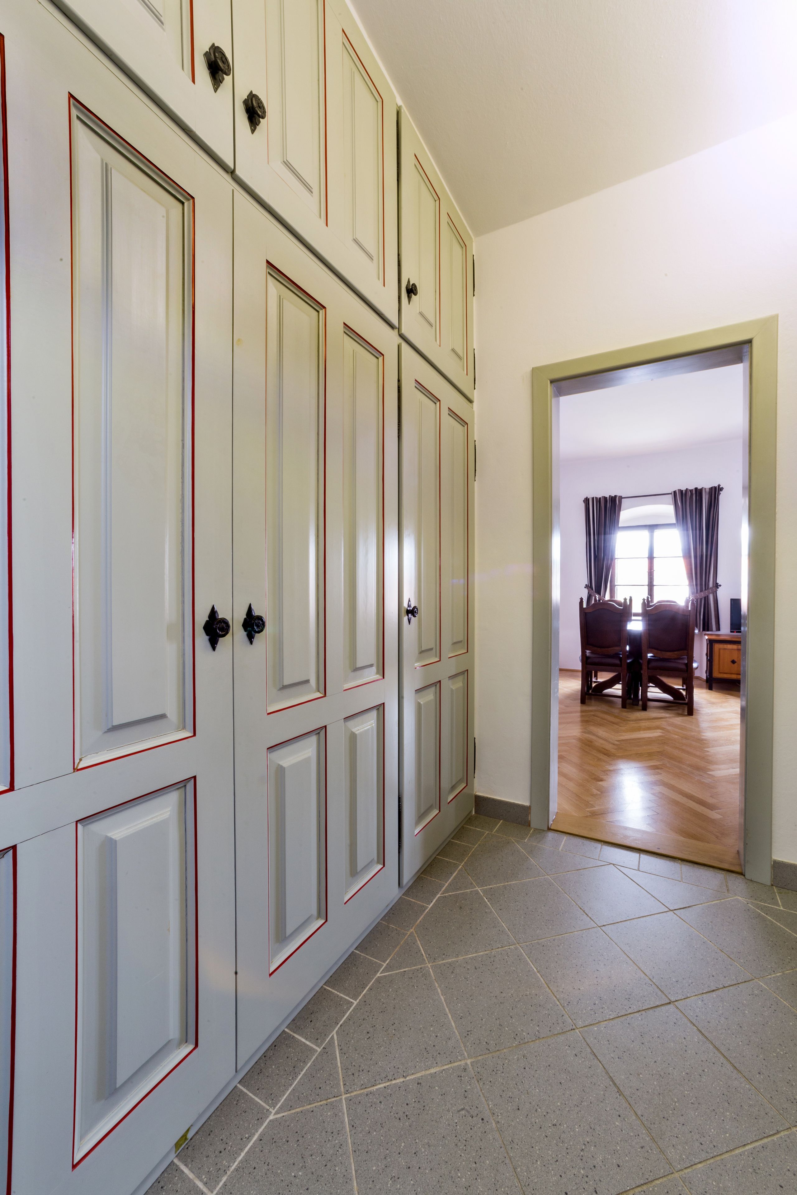 A hallway with a large wardrobe, a dining area with a table and chairs, and a window with curtains.