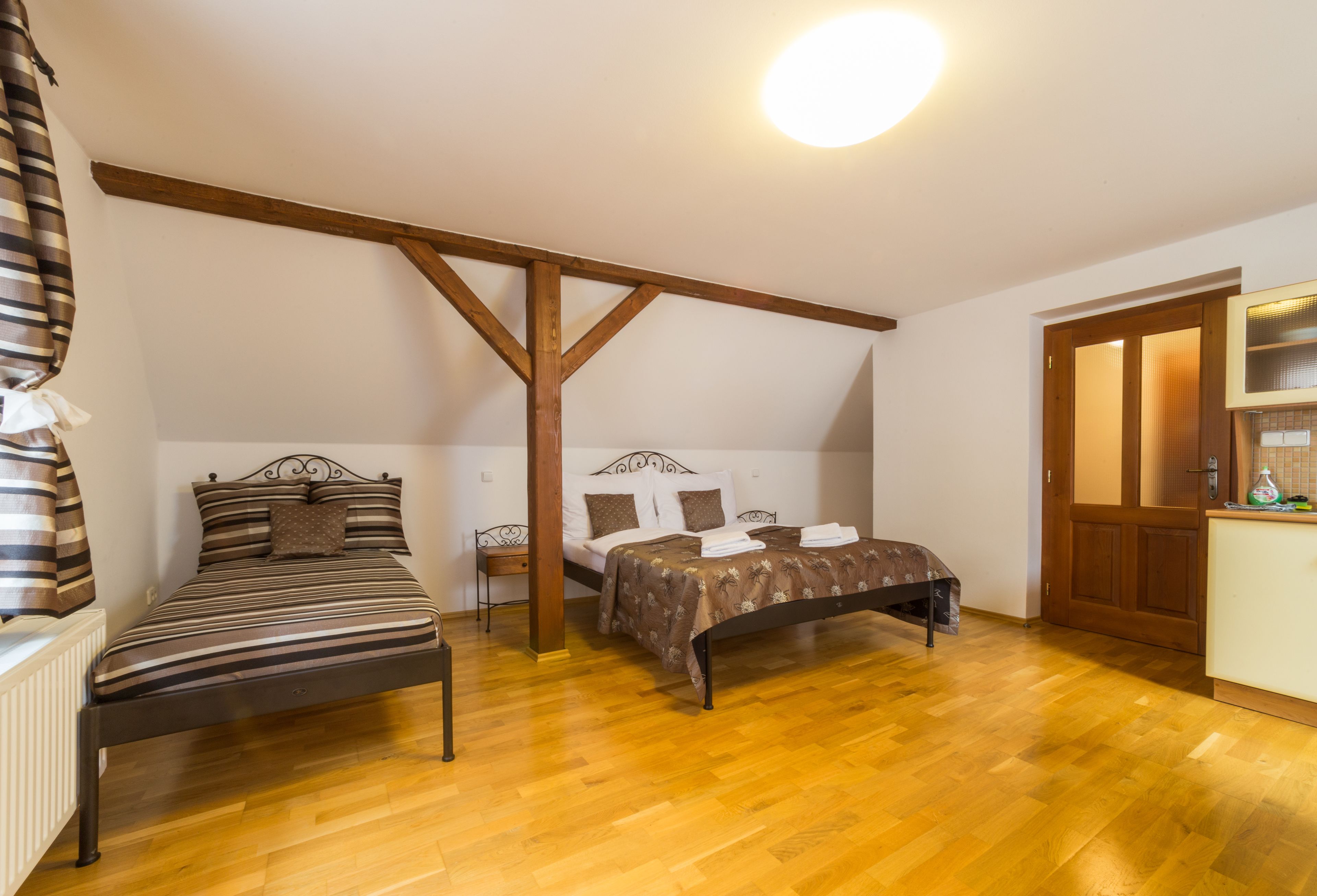 A bedroom with two beds, wooden beams, a radiator, and a wooden door.