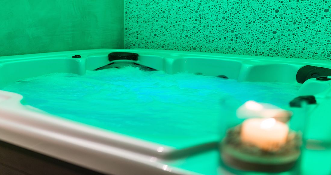 A bathtub with a green tint and a candle on a tray.