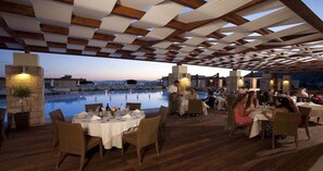 Un área de comedor al aire libre con vista a la piscina, piso de madera y una estructura de pérgola.