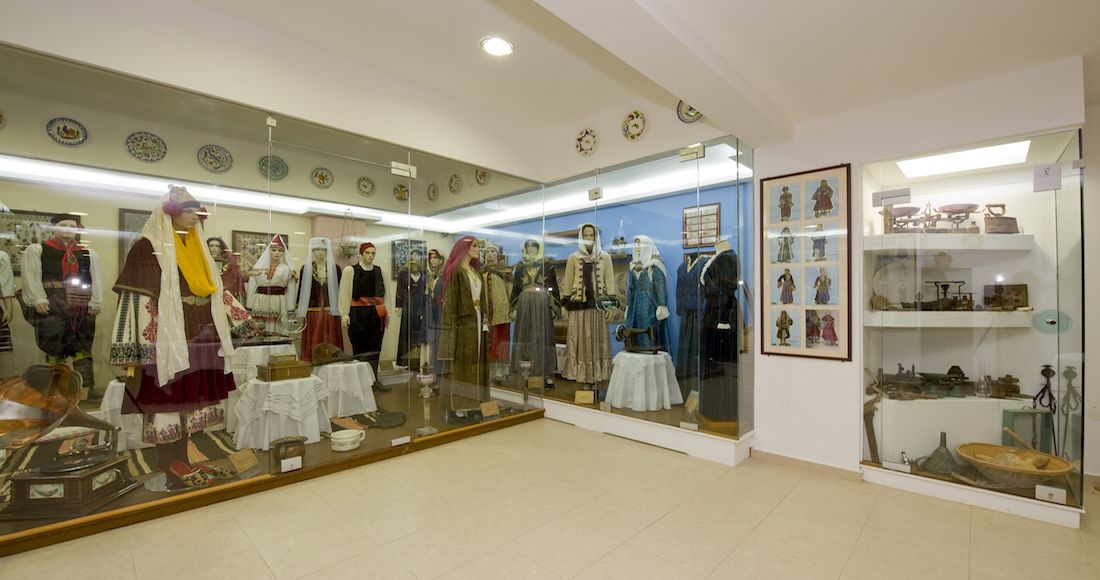 A museum exhibit with mannequins in traditional attire, glass display cases with artifacts, and a tiled floor.