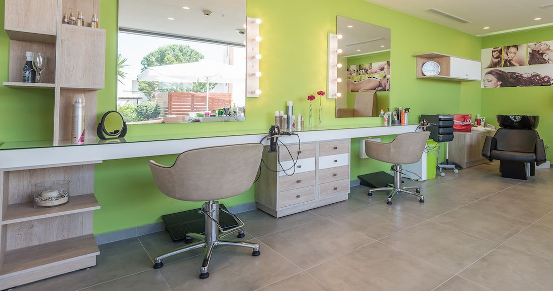 Um salão de beleza com duas cadeiras, um espelho e prateleiras com produtos para cabelo.