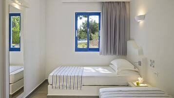 Un dormitorio con dos camas, una ventana con contraventanas azules, un espejo y una mesita de noche con una lámpara.