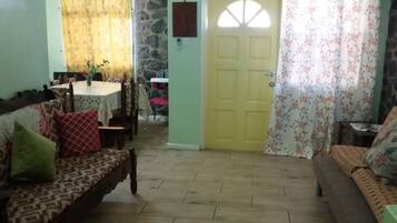 A living room with a sofa, a dining table, and a door with floral curtains.