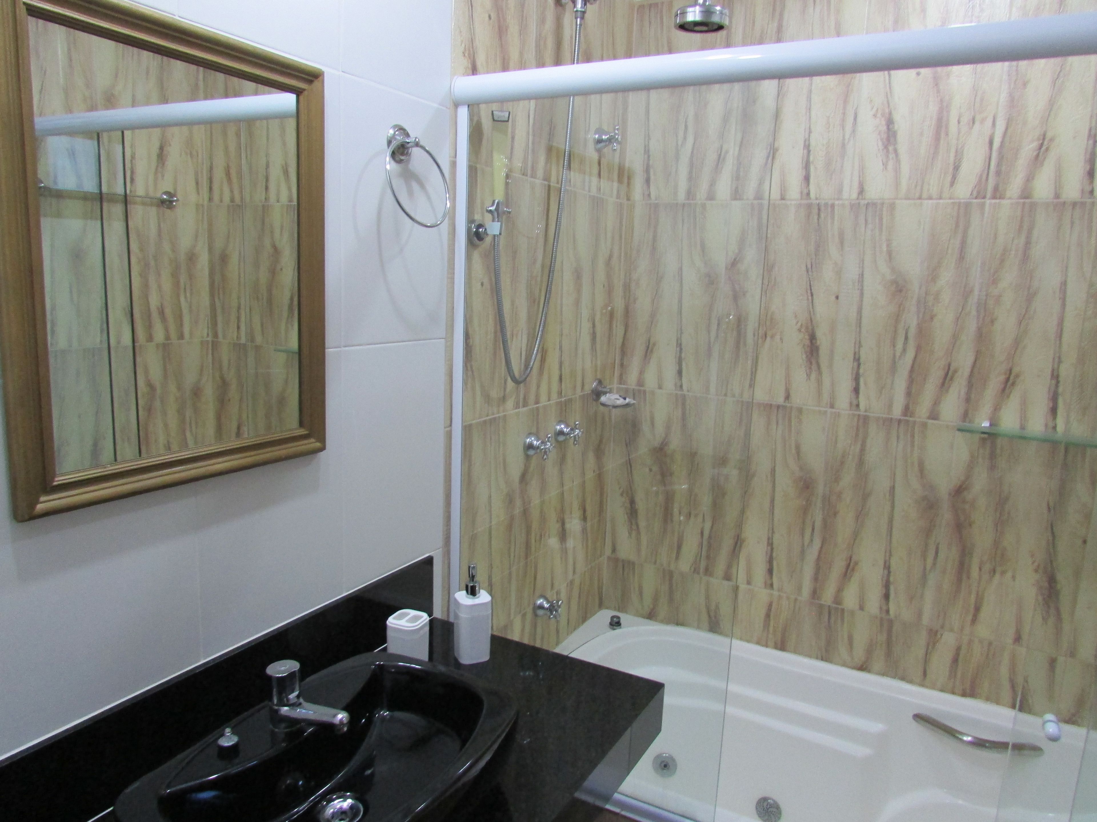 A bathroom with a black sink, a mirror, a glass-enclosed shower, and a marble-tiled wall.