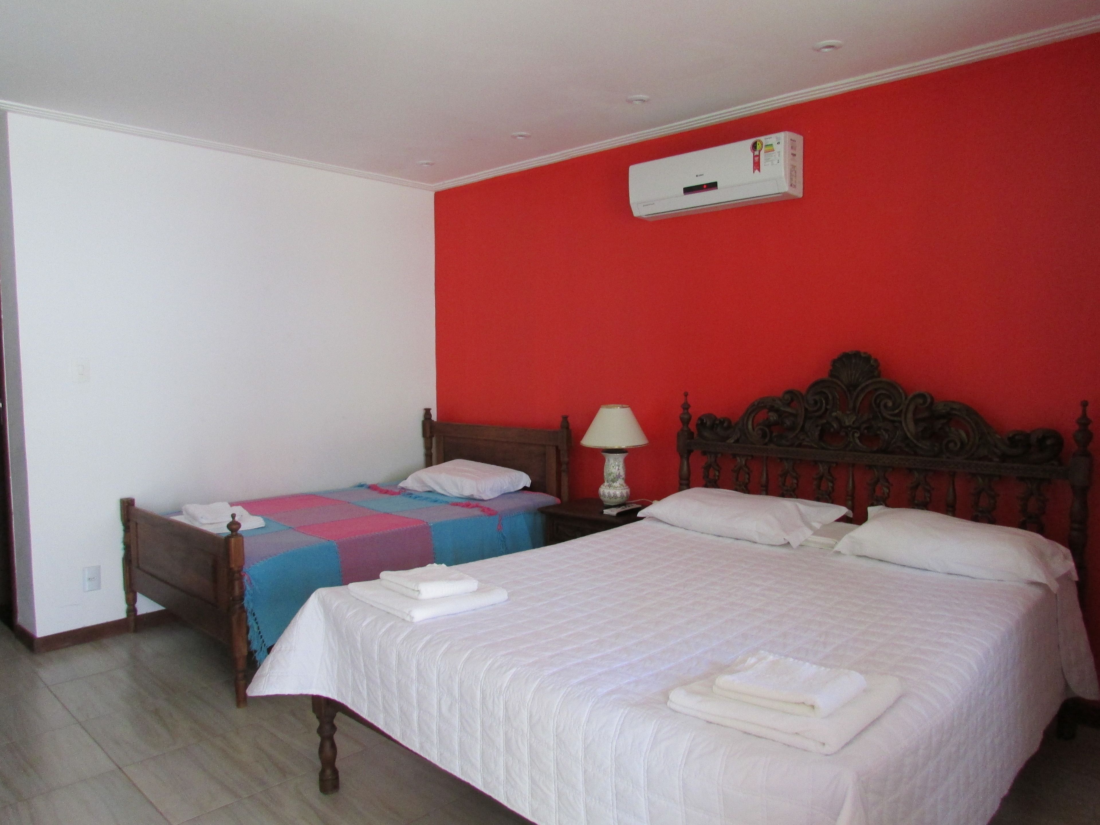 A hotel room with two beds, a red wall, and an air conditioning unit.