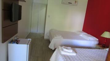 Quarto de hotel com duas camas, televisão fixada na parede, mini-geladeira e uma parede de destaque vermelha.