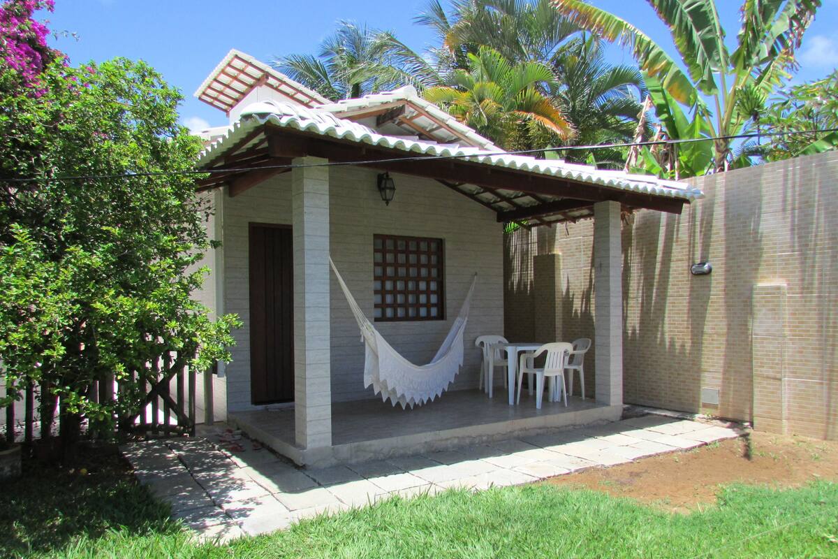 Una pequeña casa con un patio, una hamaca y una mesa con sillas.