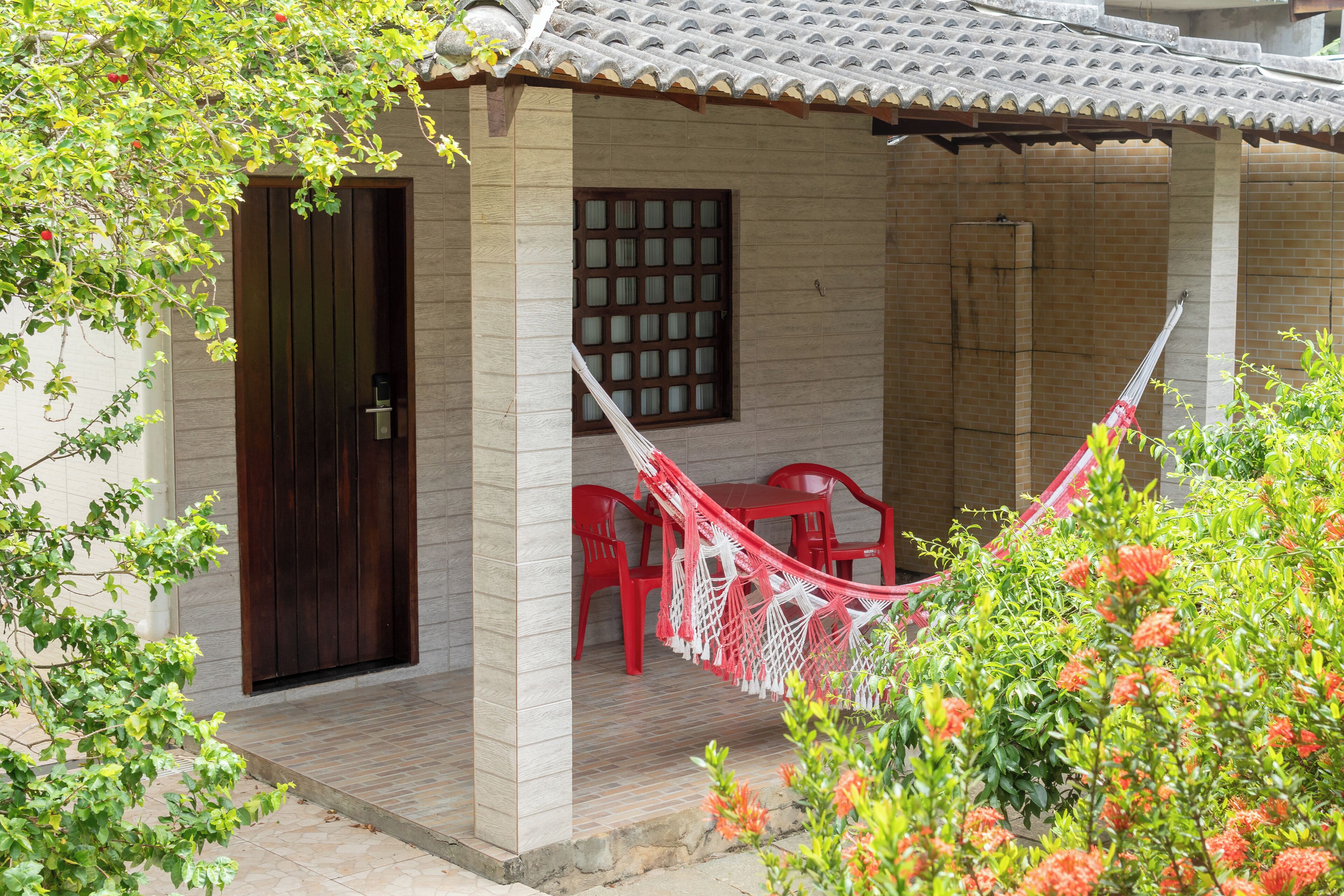 Un espace extérieur abrité, aménagé avec des sièges, un hamac, des chaises rouges et une porte en bois.