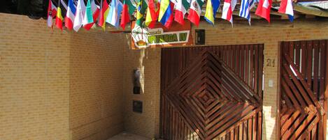 Una entrada de edificio con varias banderas nacionales, un muro de ladrillo y un gran portón de madera.