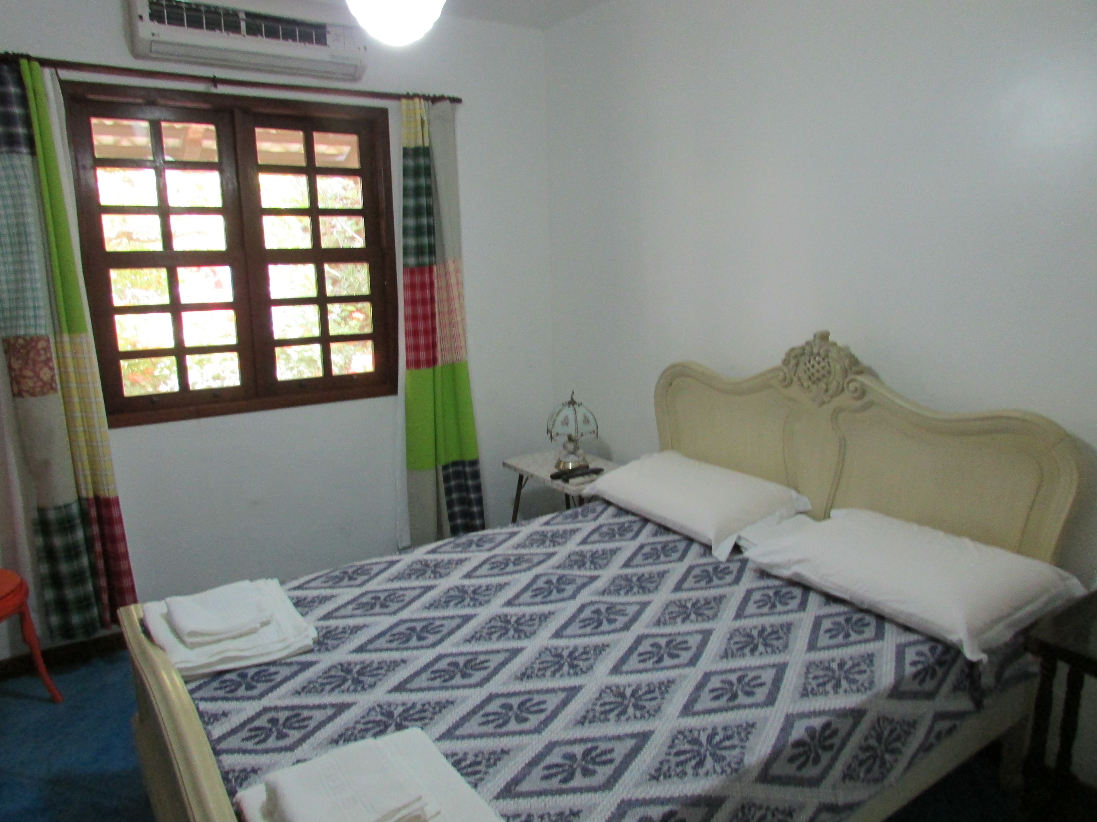 A bedroom with a bed, a nightstand, a window with curtains, and an air conditioning unit.
