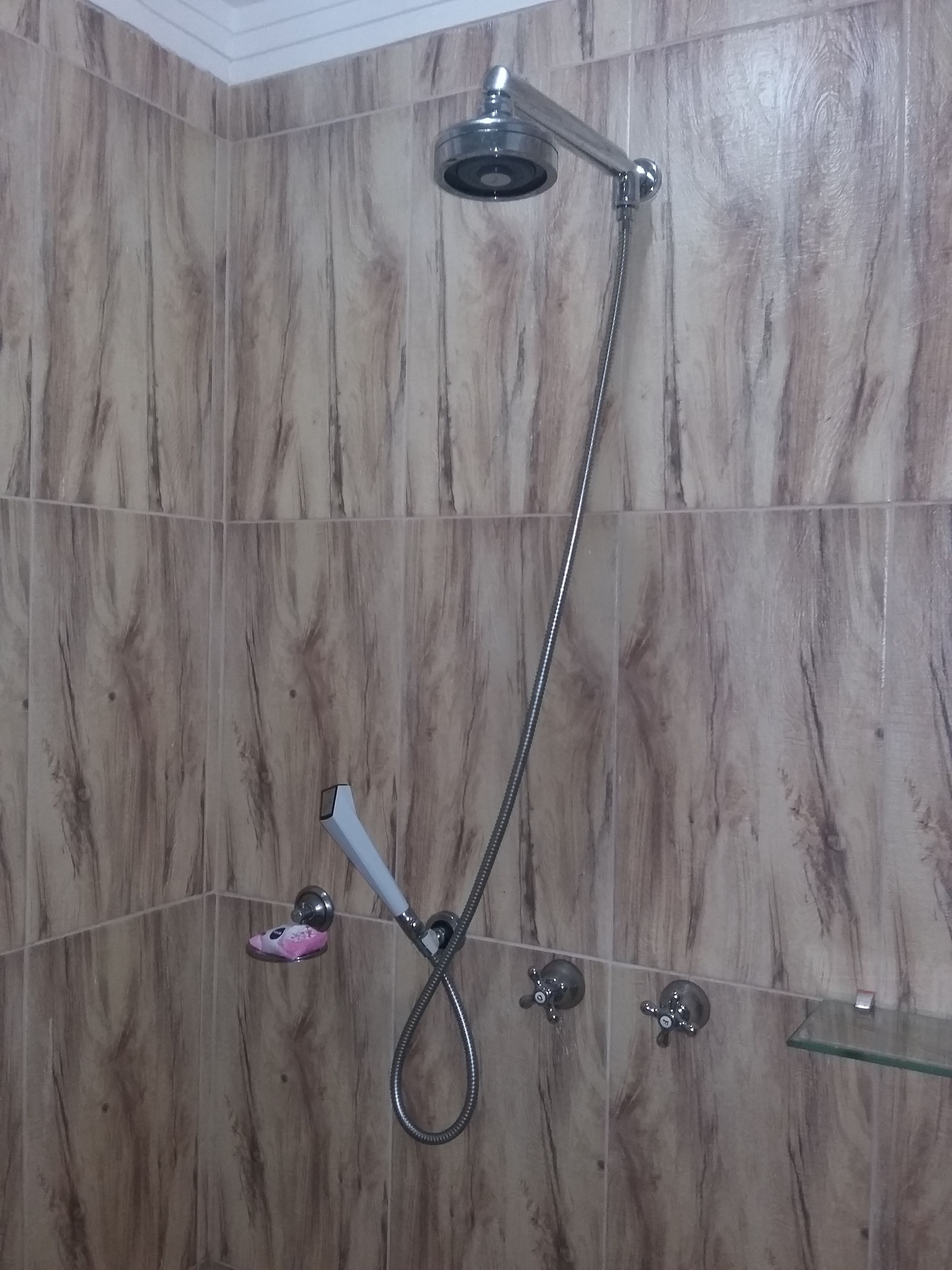 Une douche équipée d’un pommeau de douche à main et d’un robinet fixé au mur.