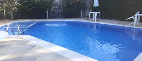 Una piscina rectangular con superficie de agua azul cristalina, rodeada por un solárium con baldosas.