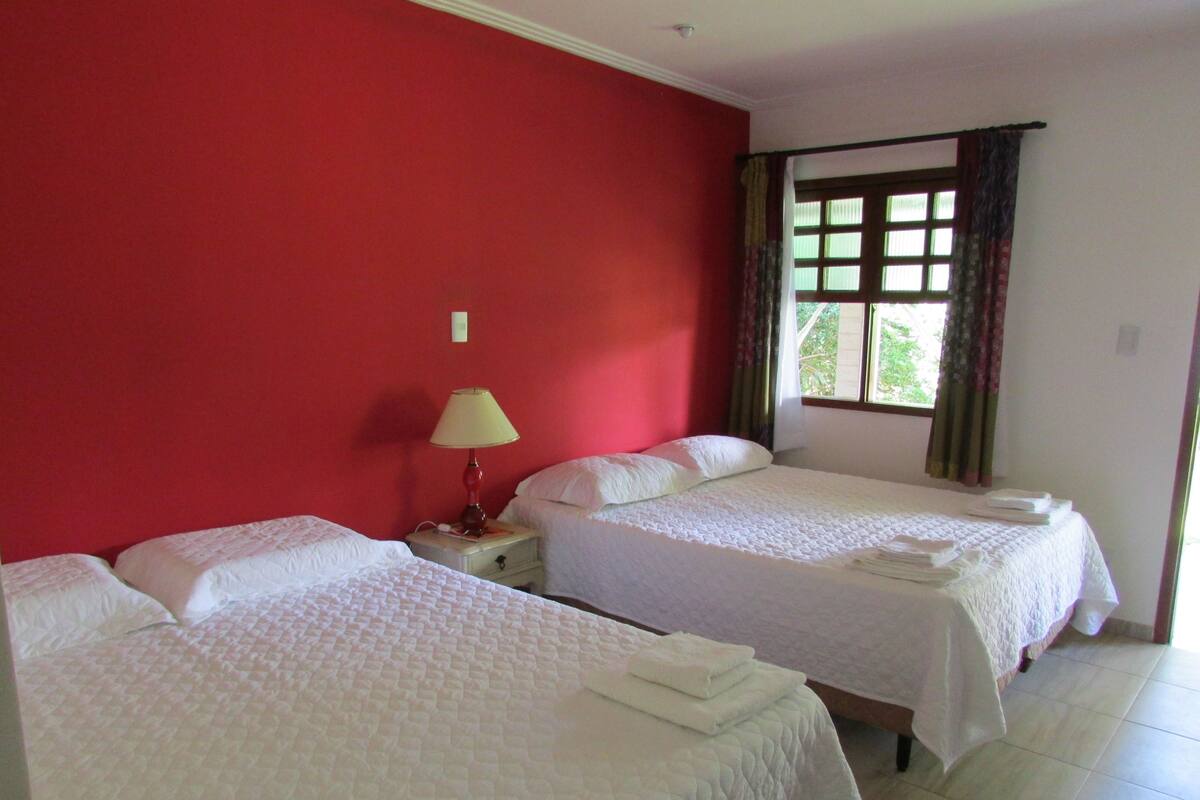 Una habitación de hotel con dos camas, una mesita de noche con lámpara y un ventanal con cortinas.