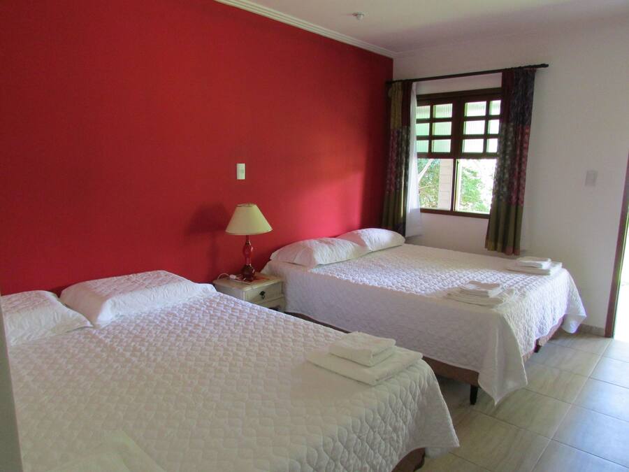 Quarto de hotel com duas camas, mesa de cabeceira com abajur e janela com cortinas.