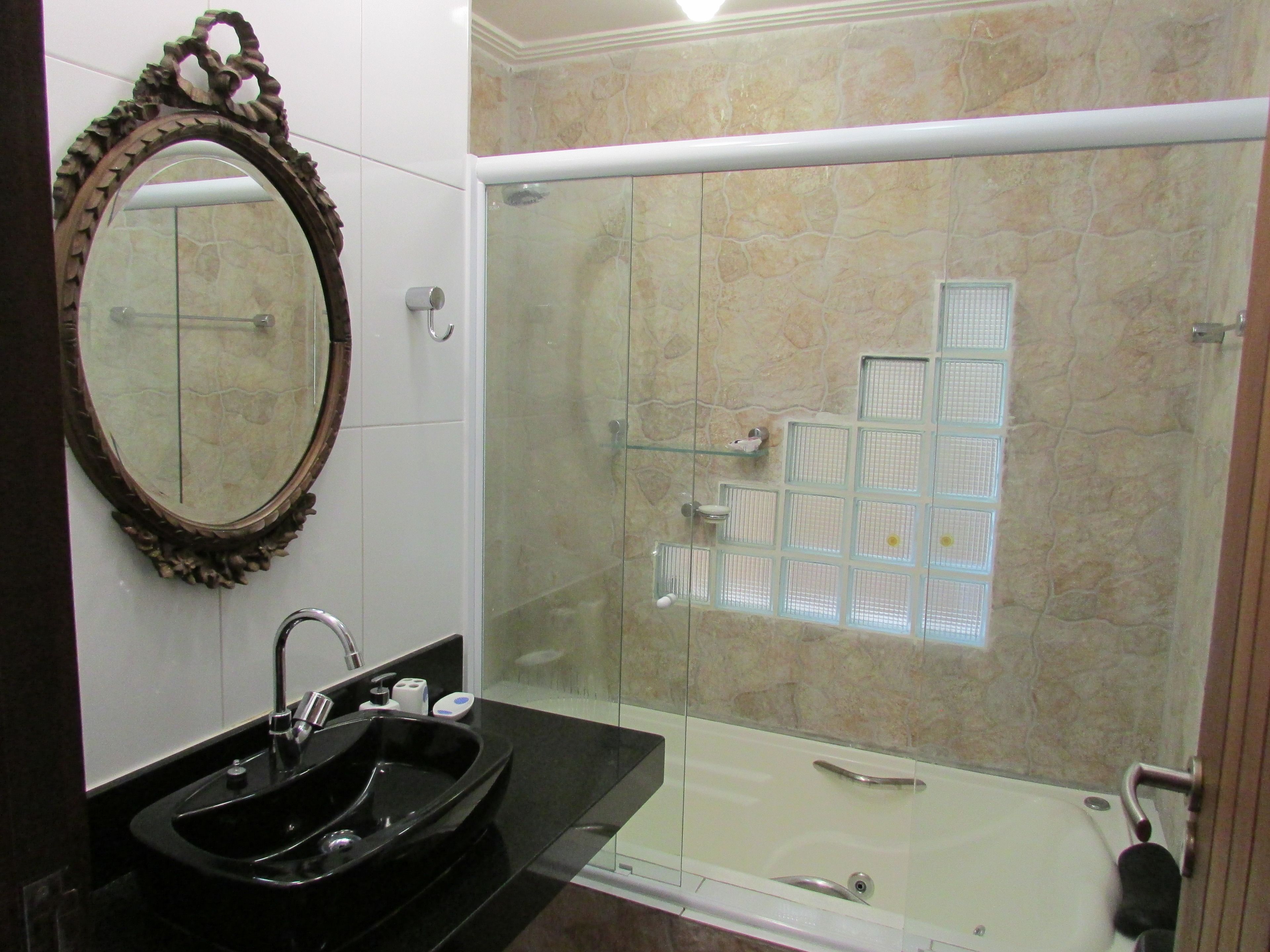 Un baño con un lavamanos negro, un espejo y una cabina de ducha con paredes de azulejos.