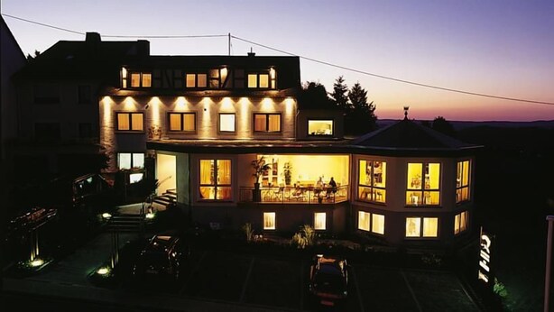 Een tweelaags huis met veel ramen en een balkon, omgeven door een oprit en een geparkeerde auto.