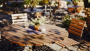 Een houten buitentafel met stoelen, een potplant en een glas water.