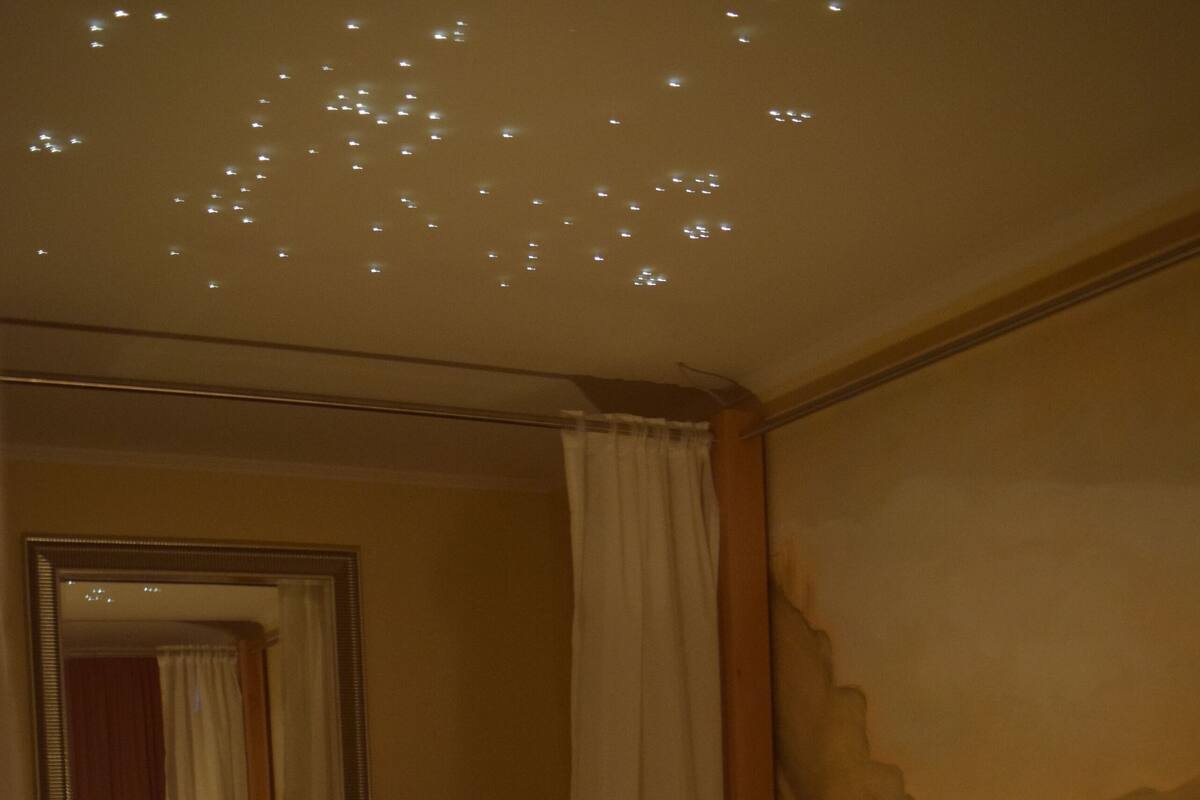 Ein schummrig beleuchtetes Hotelzimmer mit Bett, Nachttisch und einem Wandspiegel.