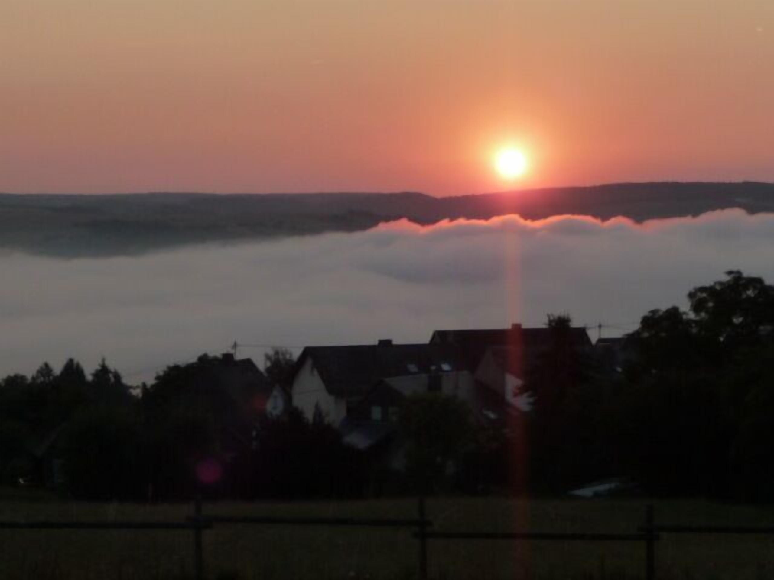 Een zonsondergang boven een woonwijk met huizen en een hek op de voorgrond.