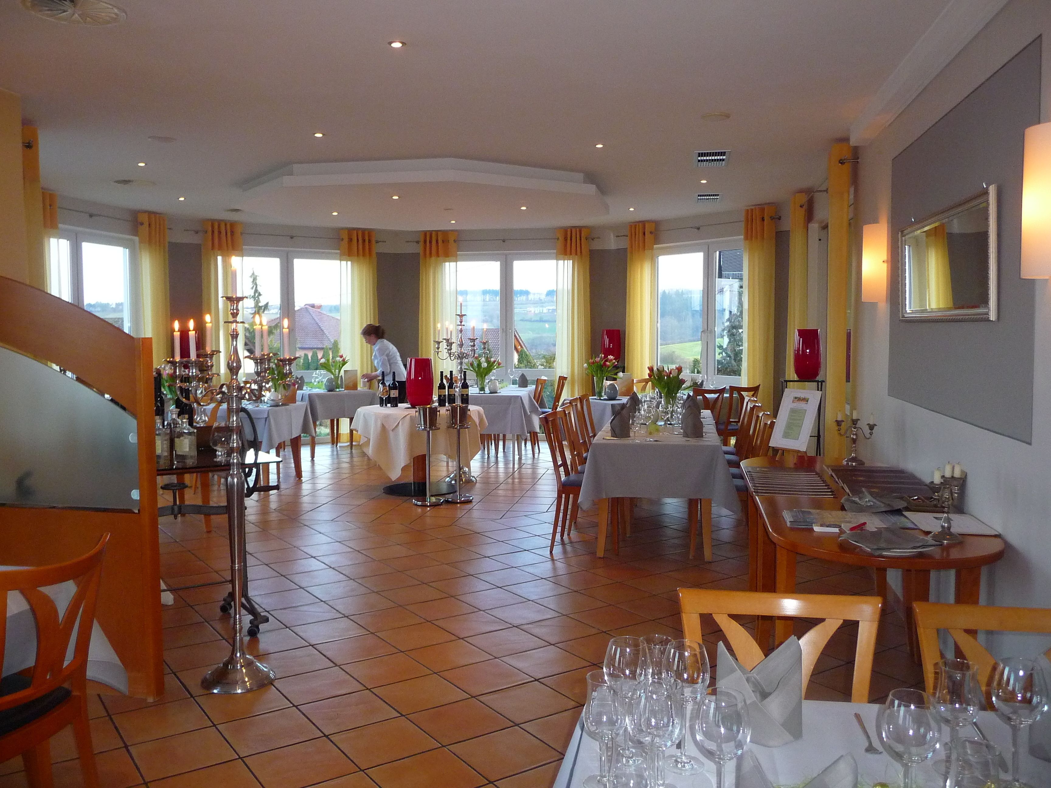 A restaurant with multiple tables set for dining, large windows with curtains, and a view of the outdoors.
