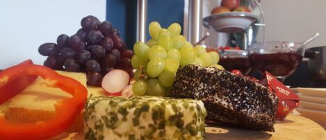 A wooden board with various cheeses, grapes, and a red bell pepper.