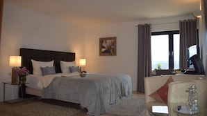 Een hotelkamer met een bed, bedlampen, een nachtkastje, een glazen tafel met een bloevas, een bank en uitzicht op de omgeving.