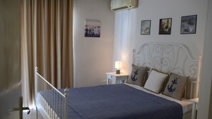 A bedroom with a bed, a nightstand, a lamp, and a wall with framed pictures. - Delfini Beach Hotel (Rhodes)