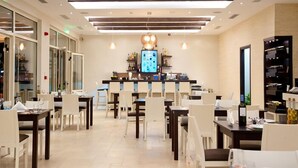 A modern dining area with a bar in the center, featuring a digital screen and a variety of bottles. - Delfini Beach Hotel (Rhodes)