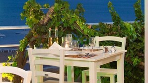 An outdoor dining area with a table set for two, overlooking a coastal view with cliffs. - Delfini Beach Hotel (Rhodes)