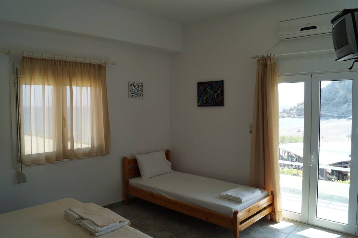 Una habitación pequeña con una cama individual, mesita de noche y ventana con cortinas.