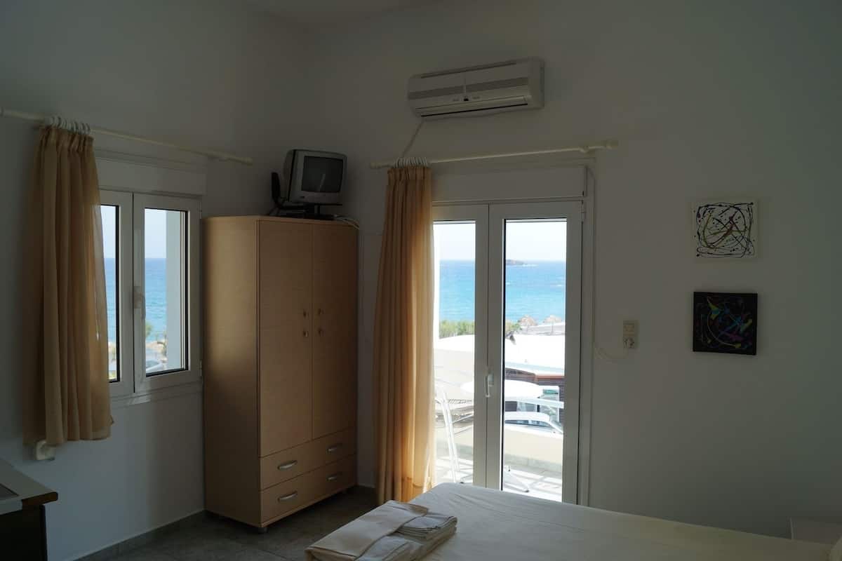 Un dormitorio con cama, armario, televisor y vista al mar a través de una puerta corrediza.