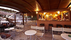 An outdoor seating area with tables and chairs, a bar with a counter and shelves of bottles, and a view of the beach. - Agia Fotia (Ierapetra)