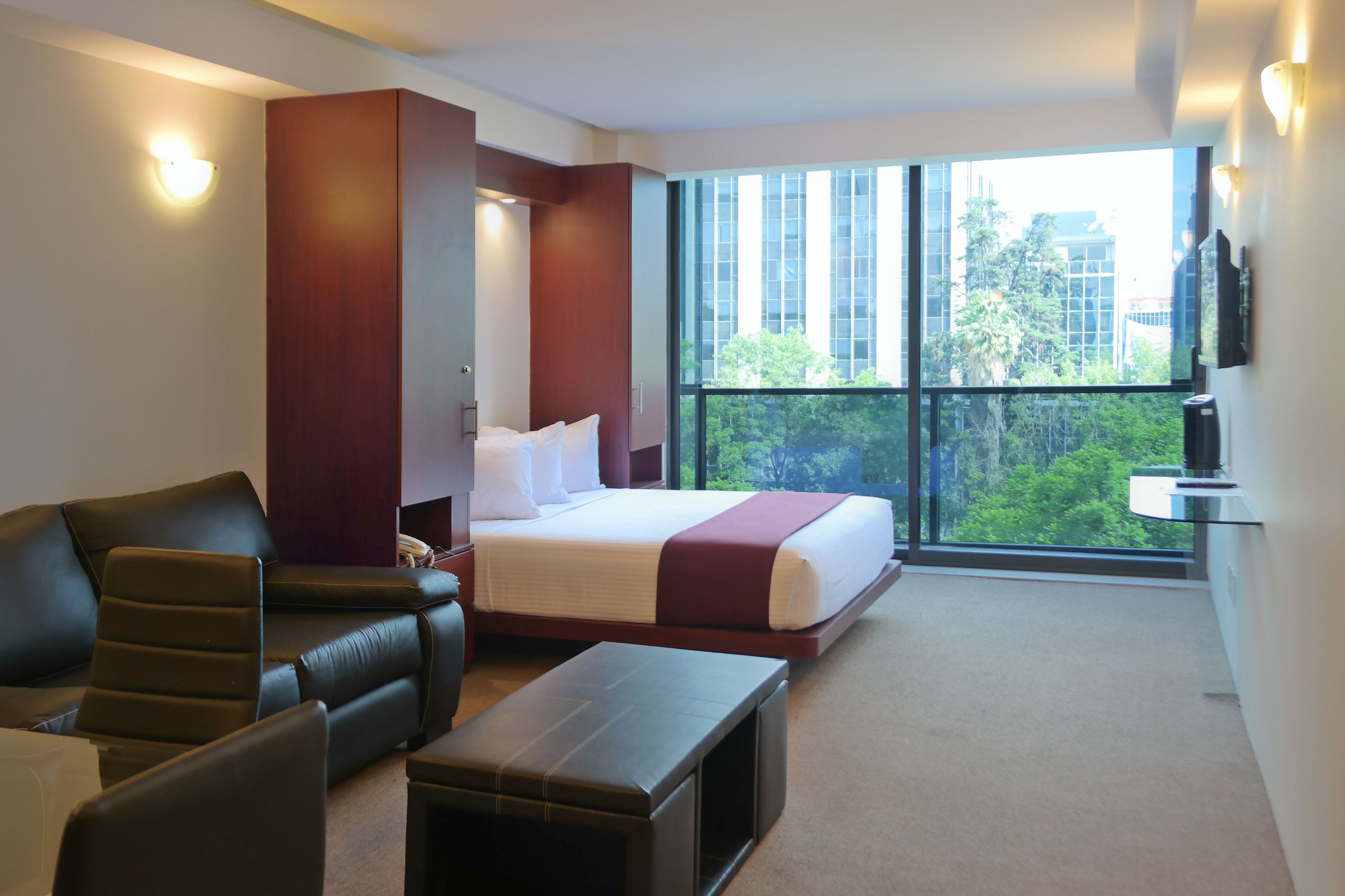 Una habitación de hotel moderna con una cama grande, un sofá, un escritorio y vistas de la ciudad a través de amplios ventanales.