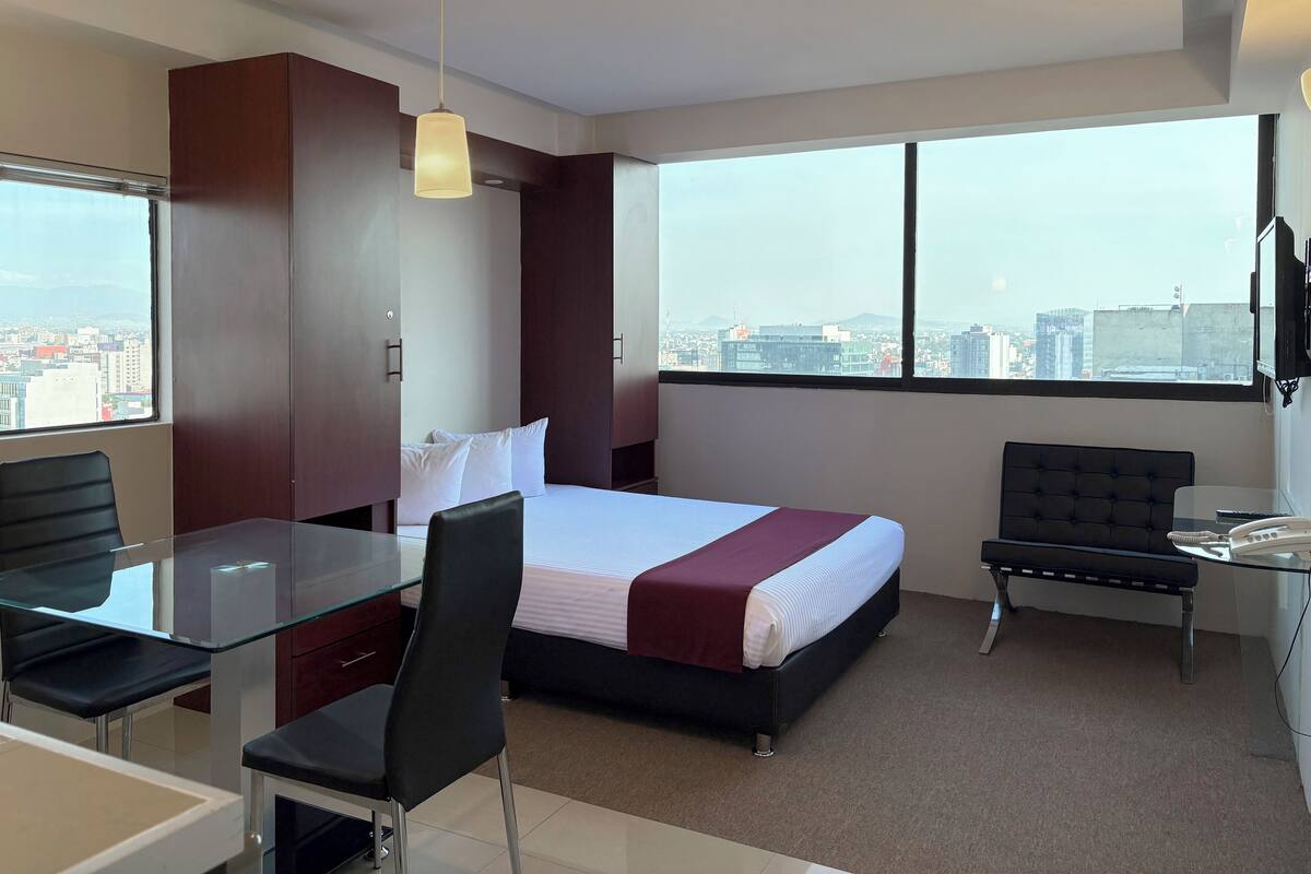 Ein modernes Hotelzimmer mit einem großen Bett, einem Schreibtisch, einem Stuhl und Blick auf die Stadt durch das Fenster.